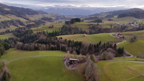 Drone-flight-over-a-hilly-landscape-in-a-cloudy-weather-with-mountains-in-the-background