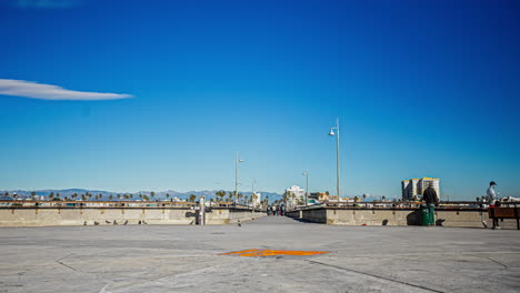 Zeitraffer-Von-Venice-Beach:-Menschen,-Die-An-Der-Promenade-Entlang-Laufen,-Mit-Blauem-Himmel-über-Ihnen