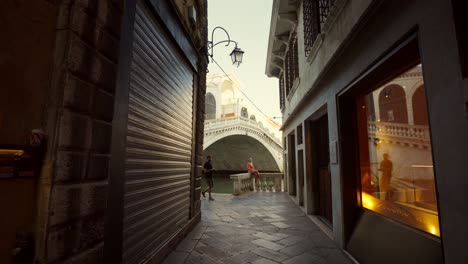 Die-Kamera-Bewegt-Sich-In-Einer-Straße-In-Venedig-Vorwärts-Und-Zeigt-Ein-Mädchen,-Das-Vor-Der-Rialtobrücke-Für-Einen-Fotografen-Posiert.