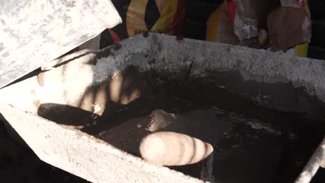 Close-up-of-water-pouring-into-a-basin-at-a-construction-site,-sunlight-casting-shadows