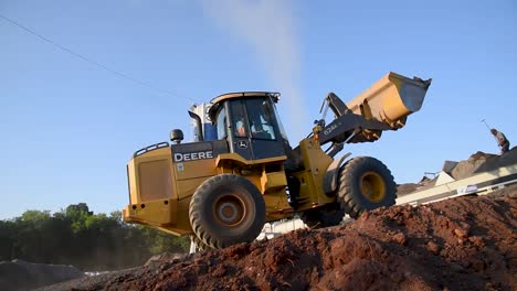 Low-angle-view-of-a-wheel-loader-at-a-construction-site-on-a-sunny-day,-dirt-in-foreground