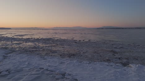 Drohnen-Dolley-Ansicht-Des-Horizonts-Mit-Sonnenuntergangsfarben-über-Einem-Zugefrorenen-See-In-Alaska