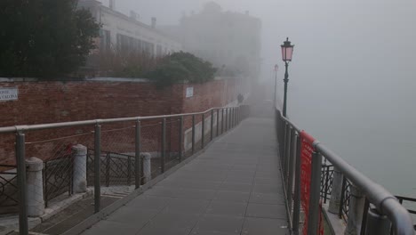 Tourist-walking-through-Foggy-Venice-Walkway-with-Bright-Blue-Suitcase