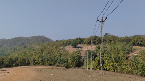 A-gentle-zoom-reveals-the-undulating-landscape-of-India,-accentuated-by-a-line-of-telephone-poles-or-power-lines