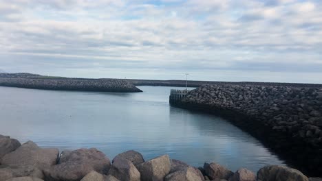 Breakwater-and-small-harbor-near-coastline-of-Iceland,-cloudy-day