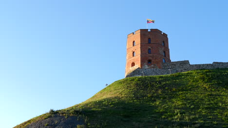 Gediminas-castle-hilltop-fortification-tower-in-Vilnius,-flying-Lithuanian-flag-under-blue-sky