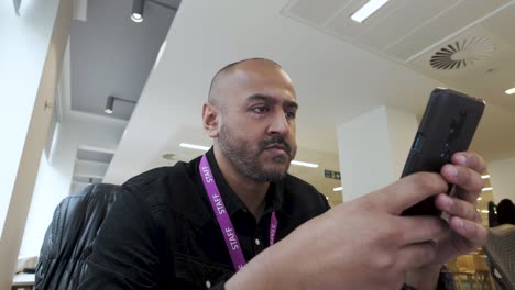 Asian-Indian-Male-in-black-shirt-using-smartphone-indoors,-focused-expression,-office-environment