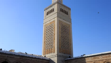 Blue-sky-over-the-ornate-facade-of-the-Grand-Mosque-of-Tunis,-with-visitors-milling-about