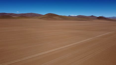 Aerial-rotates-to-reveal-rough-road-on-altiplano-desert-sand,-Bolivia