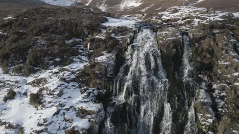 Aerial-shot-of-snowy-waterfall-in-Scotland,-cascading-among-frosted-rocks