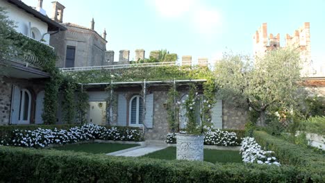 Bonito-Jardín-Bien-Cuidado-Con-Bordes-De-Flores-Blancas-Y-El-Castillo-De-Sirmione-Como-Telón-De-Fondo