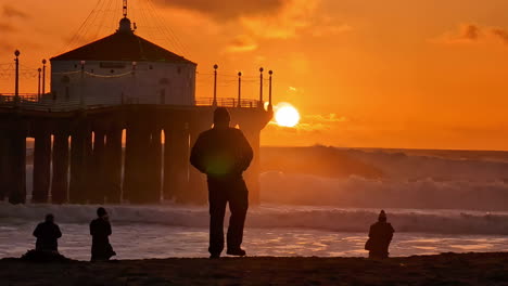 Manhattan-Beach-Sunset-Glowing-Bright-Orange-with-Ocean-Waves-and-People-Photographing-the-Roundhouse-Aquarium-Pier-with-the-Sun