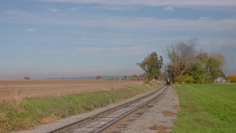 A-Track-side-View-of-a-Stem-Passenger-Train-Approaching,-Blowing-Smoke-and-Steam-on-a-Sunny-Autumn-Day