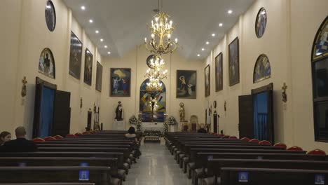 Interior-of-small-Catholic-church-with-a-sculpture-of-Christ-on-the-cross,-chandeliers-and-paintings