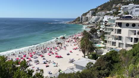 High-angle-view-of-a-busy-Clifton-Beach-and-hotels-in-Cape-Town,-South-Africa,-swimmers-and-bathers-pack-the-beach-and-waves-come-in