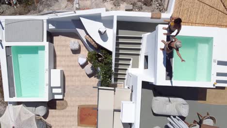Aerial-Bird-Eye-View-of-Couple-Enjoying-the-Hotel-Terrace-Accommodations,-Santorini,-Greece