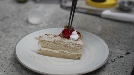 Professional-pastry-chef-places-a-cherry-on-a-piece-of-cake-preparing-a-dessert-recipe-in-the-restaurant-kitchen