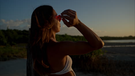 Cámara-Lenta-De-Una-Mujer-Latina-Con-Gafas-De-Sol-Mirando-La-Puesta-De-Sol-Y-Sonriendo-A-La-Cámara