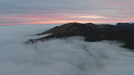 Mountain-peaks-rising-above-sea-of-clouds-during-twilight,-serene-nature-scene,-aerial-view