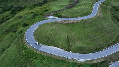 Coche-Solitario-Conduciendo-Sobre-Una-Sinuosa-Carga-De-Montaña-Rodeado-De-Prados-Verdes,-Vista-Aérea