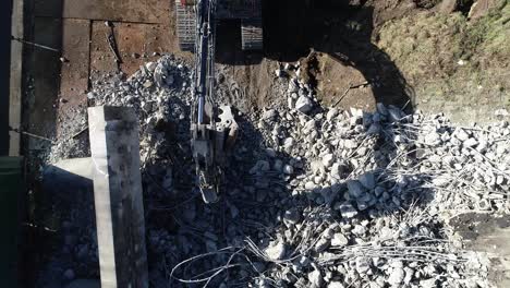 Pull-out-drone-shot-of-rubble-at-a-construction-site,-there's-an-excavator-standing-at-the-rubble