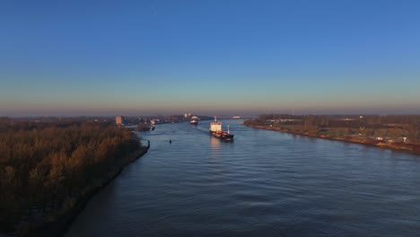 Vista-Aérea-En-Plataforma-Rodante-De-Dos-Grandes-Embarcaciones-Navegando-Sobre-Un-Río-Holandés-Durante-Un-Colorido-Amanecer