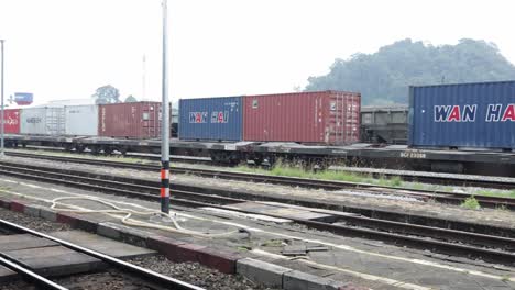 Panning-shot-of-train-wagons-carrying-cargo-containers-for-shipping-companies-parking-at-Thungsong-Junction-Railway-Station