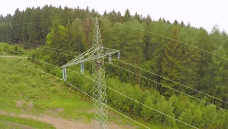 A-technician-working-on-a-high-voltage-tower-amidst-lush-green-forest,-aerial-view