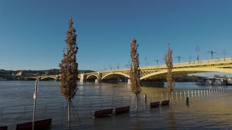 Inundaciones-Del-Río-Danubio-En-El-Puente-Margaret,-árboles-Y-Bancos-Públicos-Bajo-El-Agua---Toma-Panorámica---En-Budapest,-Hungría---28-De-Diciembre-De-2023
