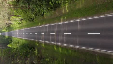 Aerial-vertical-dolly-shot-over-the-straight-asphalt-road-in-the-middle-of-the-forest-in-summer