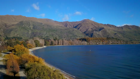 Lake-Wanaka-shoreline-New-Zealand-summer-autumn-fall-aerial-cinematic-drone-stunning-blue-sky-beautiful-morning-afternoon-Cardrona-Queenstown-South-Island-couple-walking-slowly-downward-movement