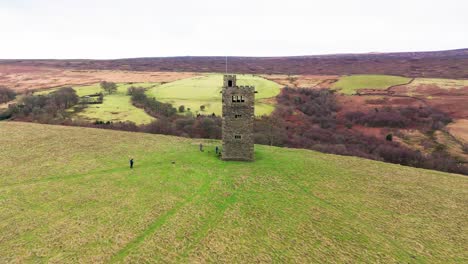 Old-derelict-castle,-monument,-disused-stone-tower,-with-people-walking-around-and-flying-a-drone
