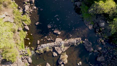 Vertical-drone-take-off-over-rock-strewn-River-Jandula,-Andalusia-landscape