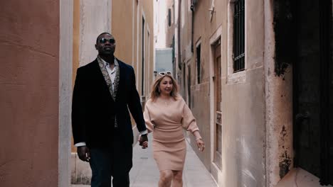 A-classy-mixed-race-couple-walking-through-the-narrow-streets-of-Venice-Italy-between-the-typical-old-houses-to-explore-the-city-while-traveling