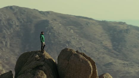 Lone-hiker-stands-atop-a-mountain-peak-fast-parallax-drone-shot