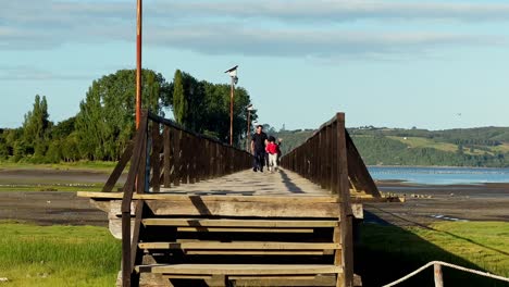Family-strolling-along-wooden-walkway-bridge-from-Aucar-Island,-Natural-Scenery,-Chile
