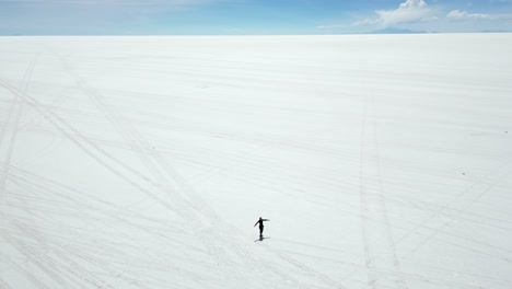 Aerial-orbits-lone-person-in-vastness-of-Uyuni-salt-flat-lake,-Bolivia