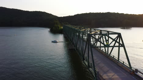 Motorboot-Fährt-Bei-Sonnenuntergang-Unter-Einer-Straßenbrücke-über-Die-Wasseroberfläche-Hindurch