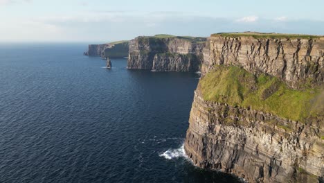 The-majestic-cliffs-of-moher-on-ireland's-coastline,-sailboat-in-the-water,-daylight,-aerial-view