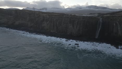 Kilt-Rock-Und-Mealt-Falls-Auf-Der-Isle-Of-Skye,-Schottland-Mit-Meereswellen-Und-Schneebedeckten-Bergen-Im-Hintergrund,-Luftaufnahme