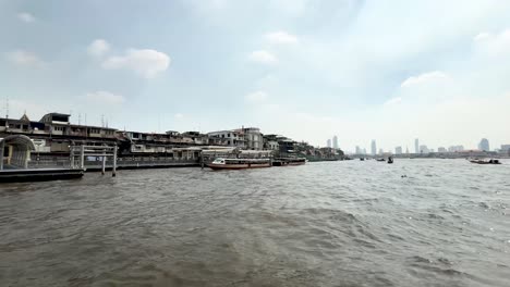Chao-Phraya-River-tour-boat-with-city-and-other-boats-in-Bangkok-Thailand,-View-from-water-transport-shot
