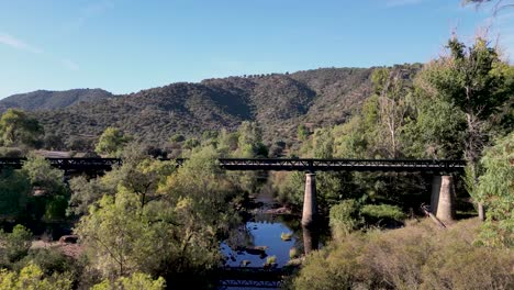 Car-crossing-bridge-over-River-Jandula,-remote-Sierra-de-Andujar-forested-landscape-DRONE-PUSH