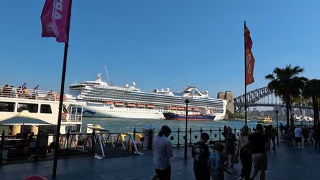 Crucero-Atracado-En-El-Puerto-De-Sydney-Con-Gente-Y-El-Puente-Del-Puerto-De-Sydney-En-El-Fondo,-Día-Soleado