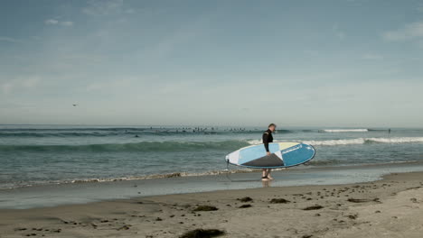 Un-Surfista-Mayor-Sube-Por-La-Playa-En-Una-Playa-Cerca-De-Cardiff,-California