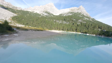 Person-walking-near-light-blue-mountain-lake-in-Dolomites,-extreme-fast-fly-by-view