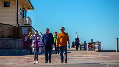 People-sightseeing-along-boardwalk-promenade-on-California-coastline,-time-lapse