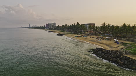 Negombo-Sri-Lanka-Aerial-v4-low-drone-flyover-along-the-coastline-of-Wellaweediya-beach-capturing-beachfront-houses,-calm-waters,-sandy-beach-and-golden-sunrise---Shot-with-Mavic-3-Cine---April-2023