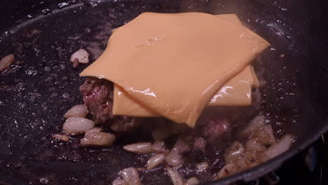 Cheese-slices-added-to-hamburger-in-pan,-cooked-with-onions,-closeup