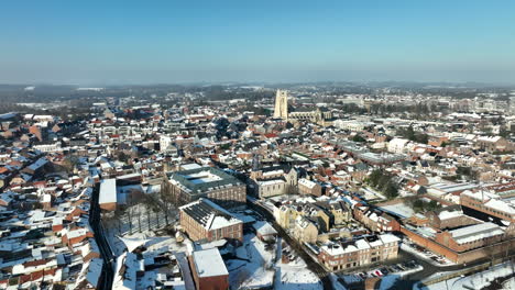 Aerial-flying-over-Tongeren-city-in-sunny-winter-day,-roofs-with-snow,-Belgium