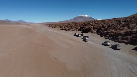 Tourism-trucks-stop-on-Bolivian-altiplano-desert-by-eroded-rock-bluff